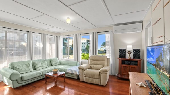A living room with a sofa, armchair, coffee table, TV, speakers, and a view of the outside. - Kitchener Street 2, Golden Beach (Golden Beach)