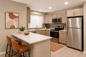 A modern kitchen with a central island, stainless steel appliances, and wooden cabinets. - Montvale Urban Suites (Toronto)