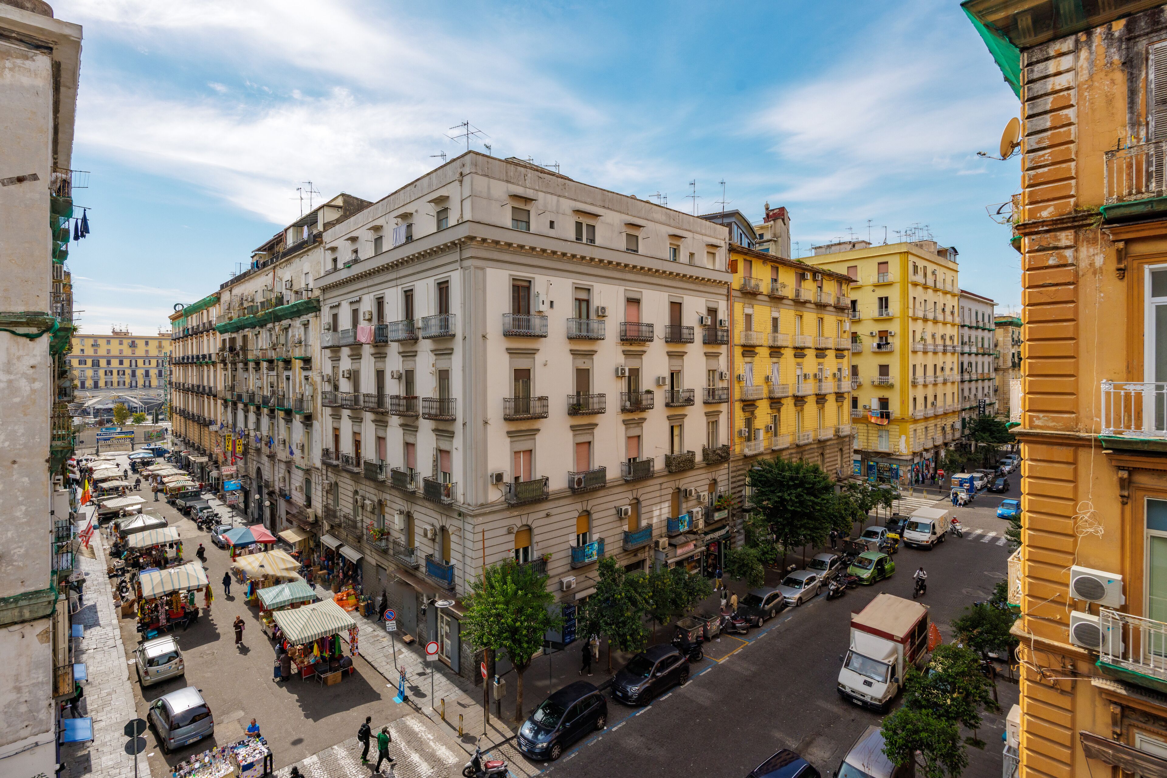 A multi-story building with balconies, a street market, and parked vehicles.