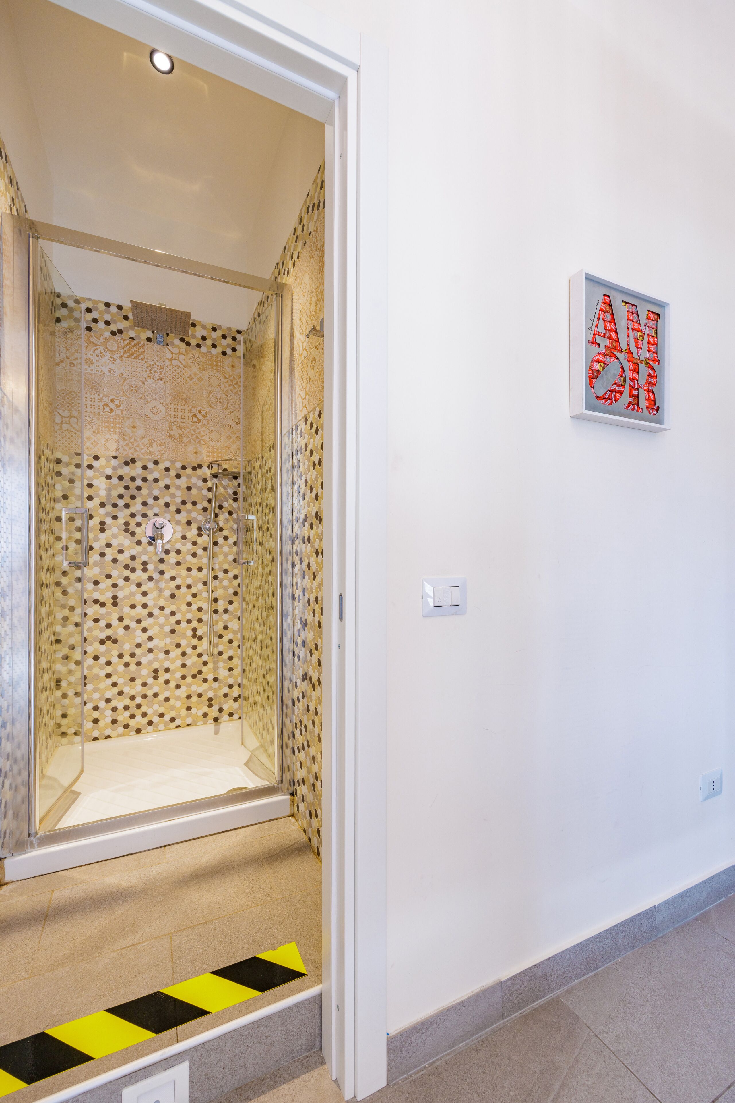 A shower with a patterned tile wall and a glass door.