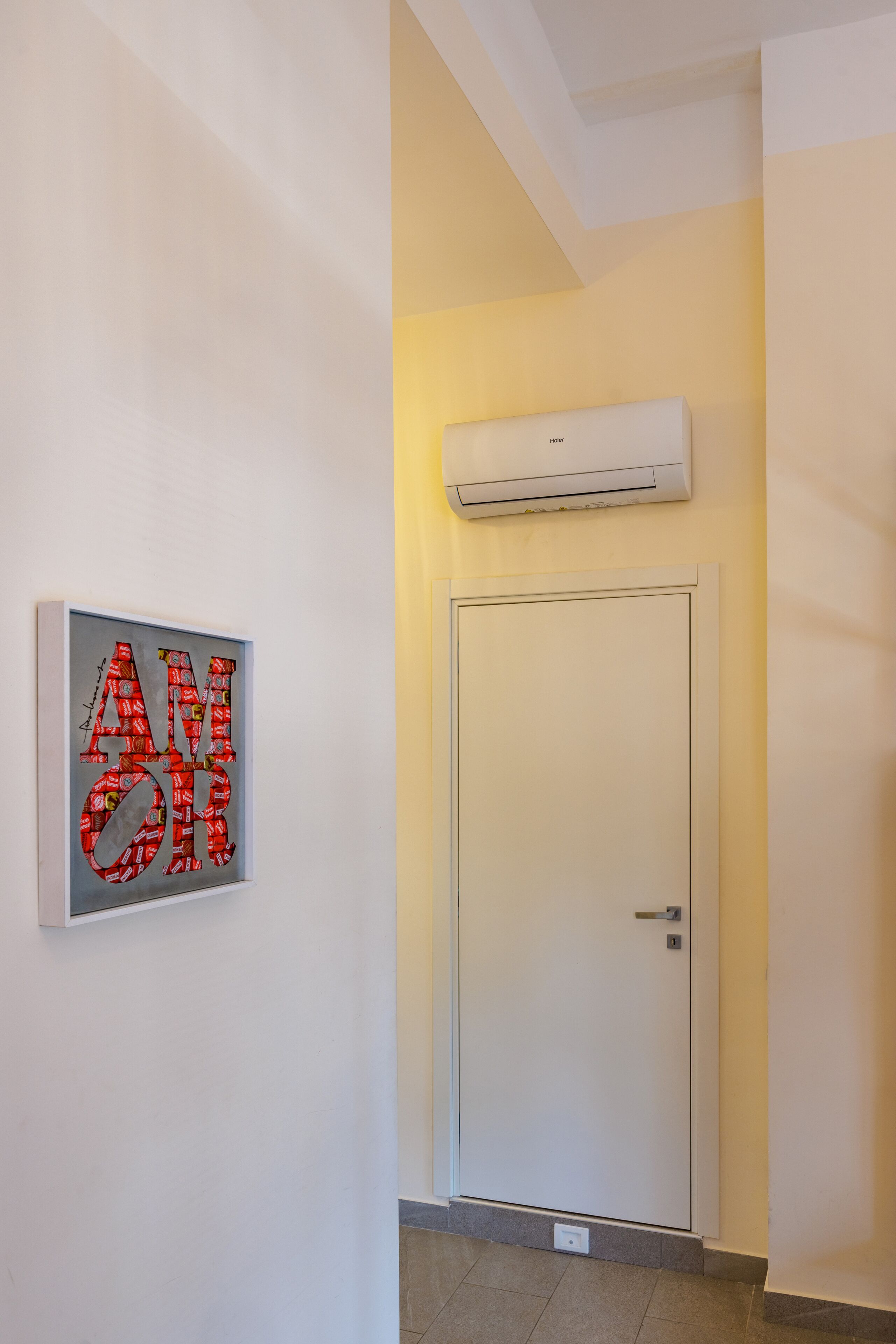 Een gang met een gekaderd kunstwerk, een gesloten deur en een airconditioner aan de muur.