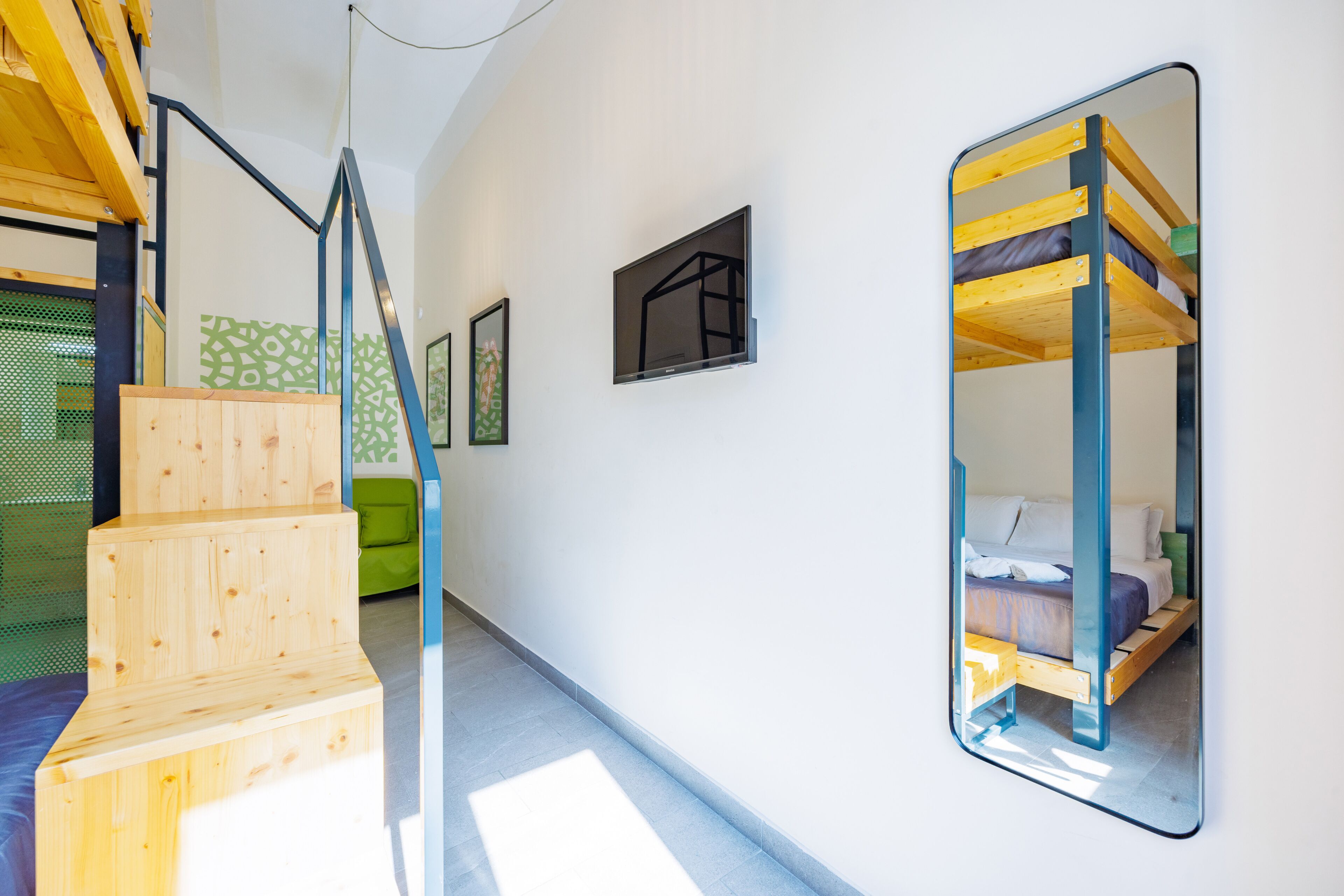 Un intérieur moderne avec un lit superposé, des marches en bois et un miroir qui reflète la pièce.
