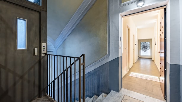 Una escalera con barandilla de metal que lleva a un pasillo con suelo de madera y una puerta al final.