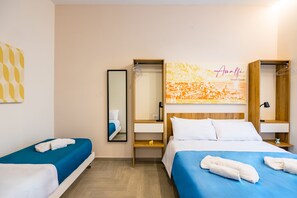 A hotel room with two beds, a mirror, a wardrobe, and a wall with a cityscape artwork. - Glow Tripla - Solaris Suites (Naples)