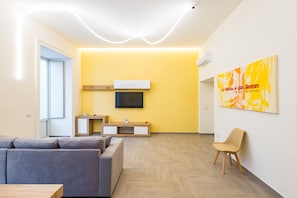 A modern living room with a sofa, a TV, a wooden cabinet, and a chair. - Solaris Suites by Napoliapartments (Naples)