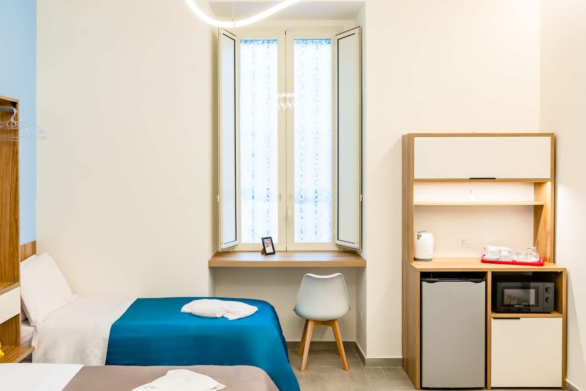 A hotel room with a bed, a desk, a chair, a wardrobe, and a small kitchenette.
