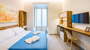 Habitación de hotel con cama, escritorio, silla, televisor y ventana.
