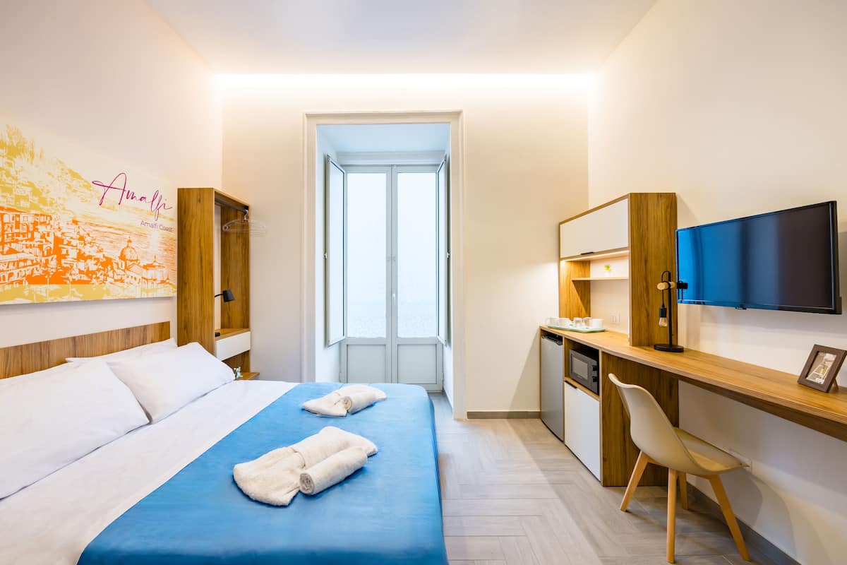 A hotel room with a bed, a desk, a chair, a TV, and a window.