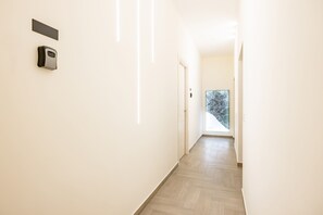 A hallway with a door, a wall-mounted device, and a window with a view of trees. - Solaris Suites by Napoliapartments (Naples)