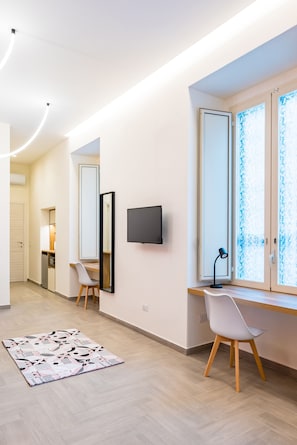 Moderni hotellihuone, jossa on työpöytä, tuoli, televisio ja suuret ikkunat.