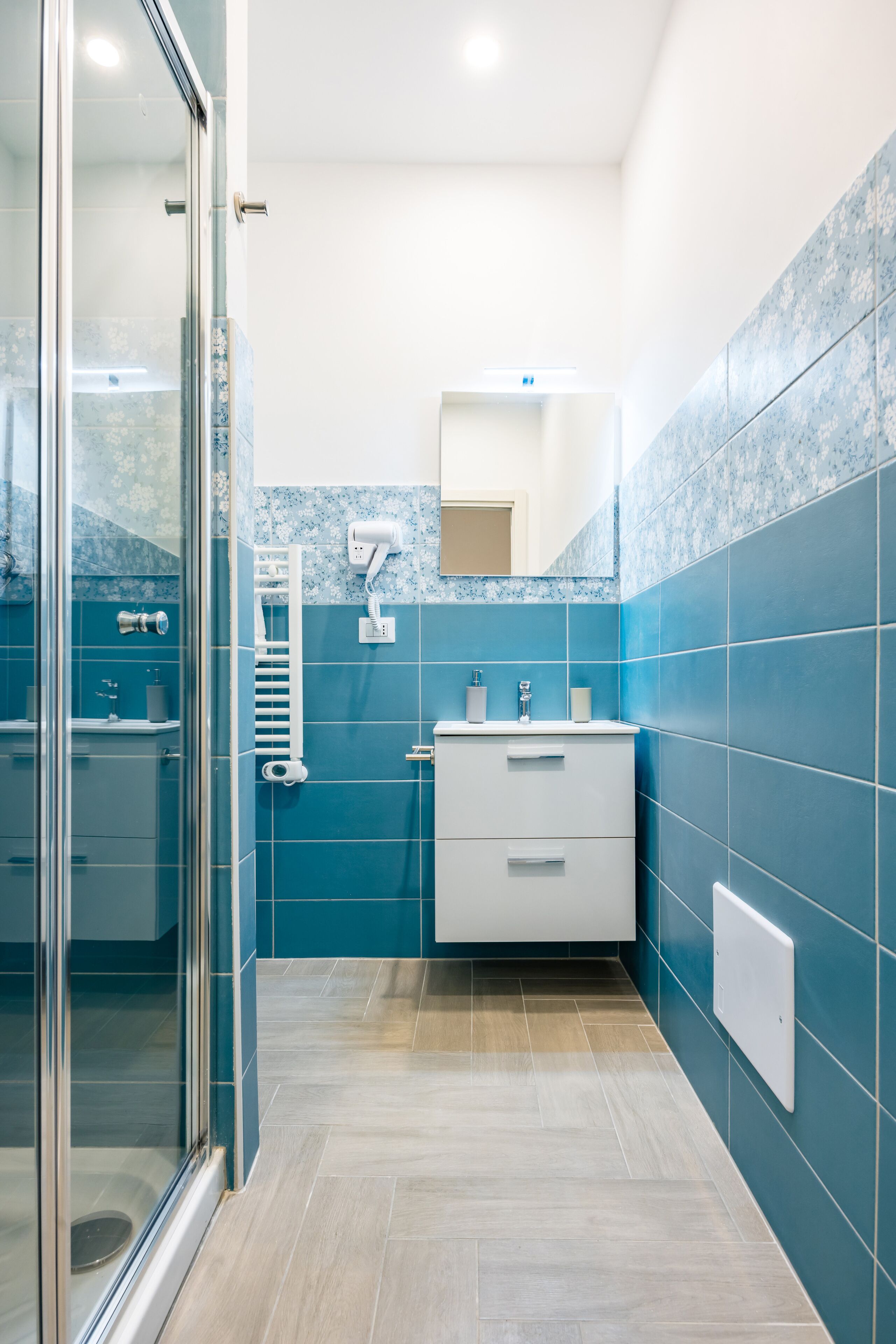 A modern bathroom with a glass shower enclosure, a white vanity with a mirror, and blue-tiled walls.