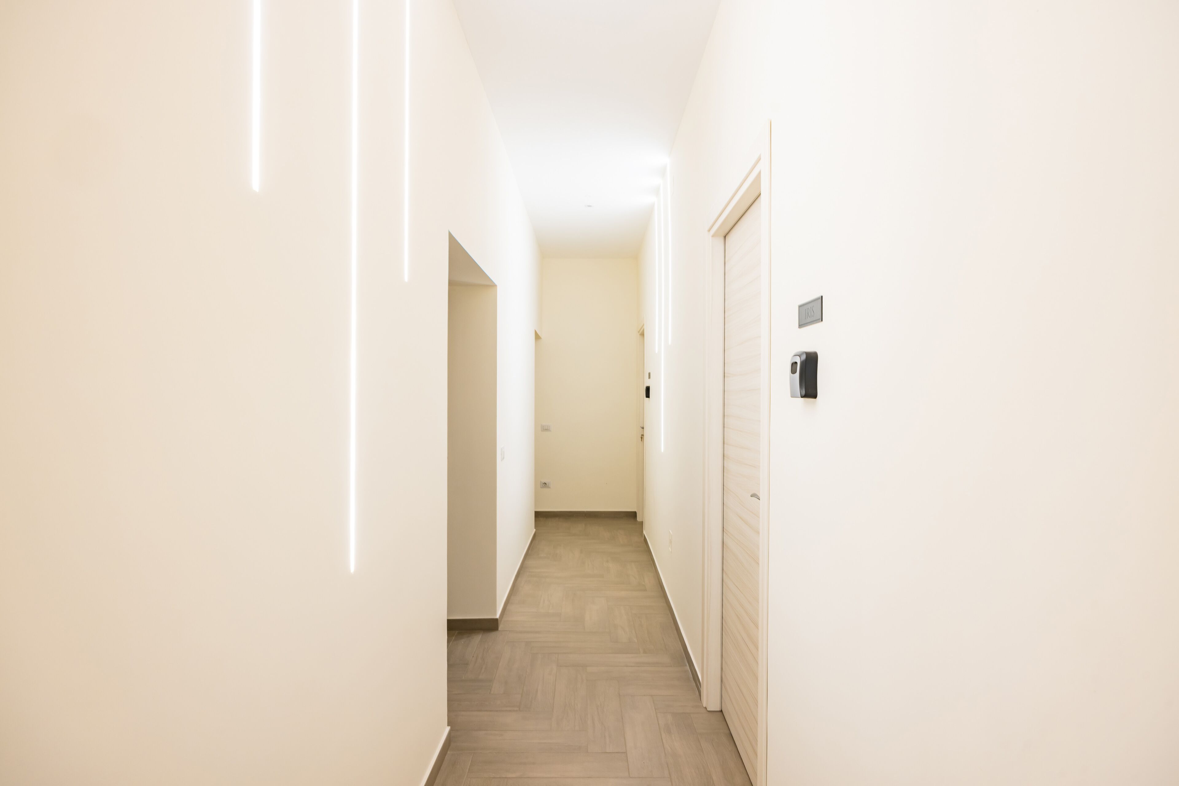 A narrow hallway with a wooden floor, white walls, and a door on the right.