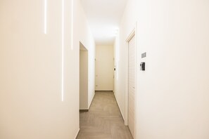 Um corredor estreito com piso de madeira, paredes brancas e uma porta à direita.