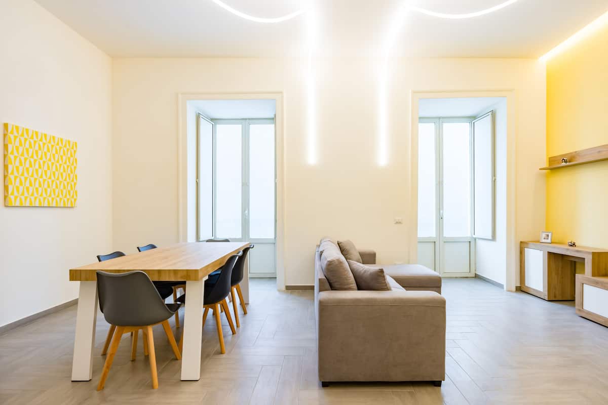 A modern living room with a wooden dining table, a sofa, and a reception desk.