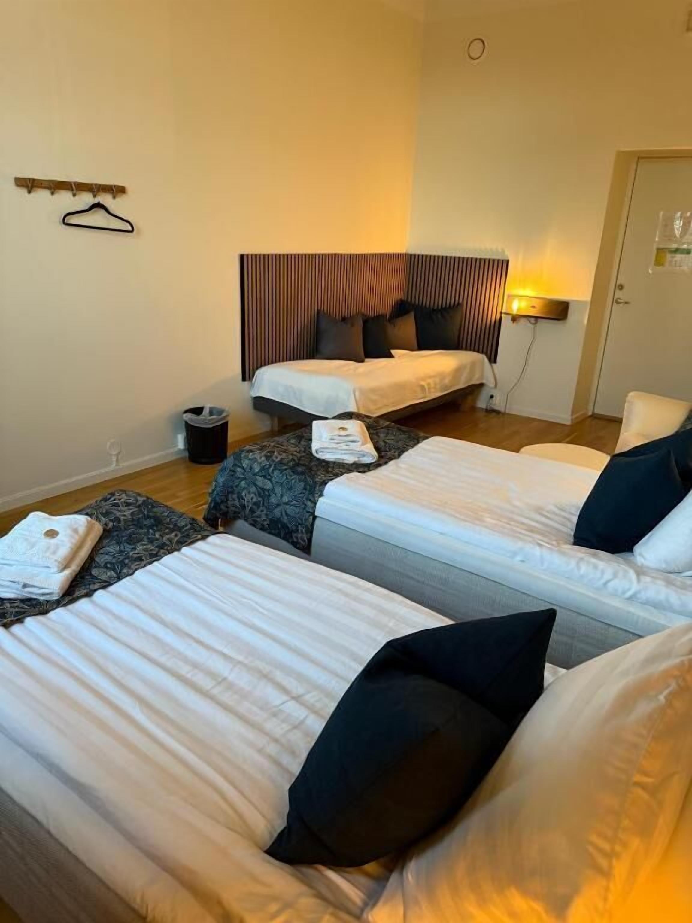 Habitación de hotel con dos camas, una mesita de noche, una lámpara y una puerta.