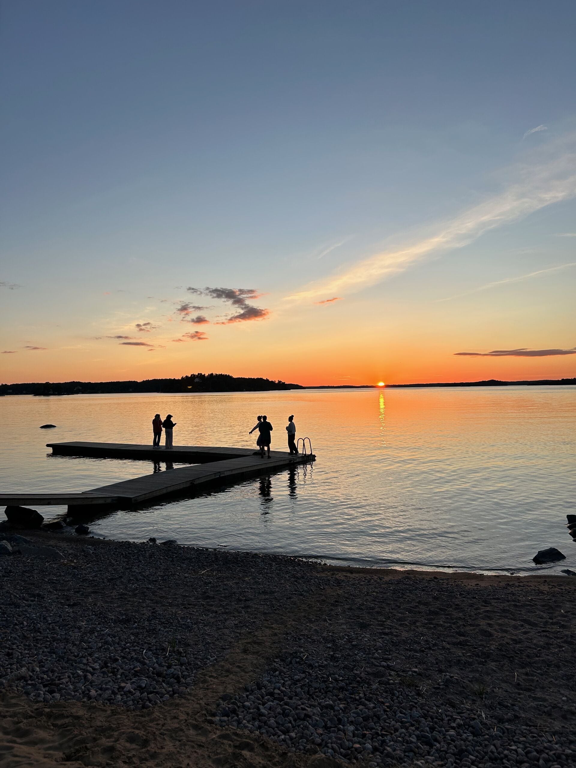 A sunset over a calm lake with a wooden dock extending into the water.