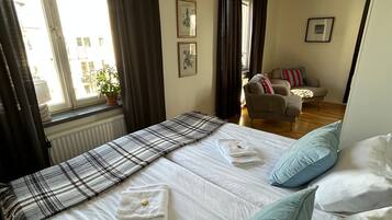 Quarto de hotel com cama, poltrona, janela com cortinas e radiador.
