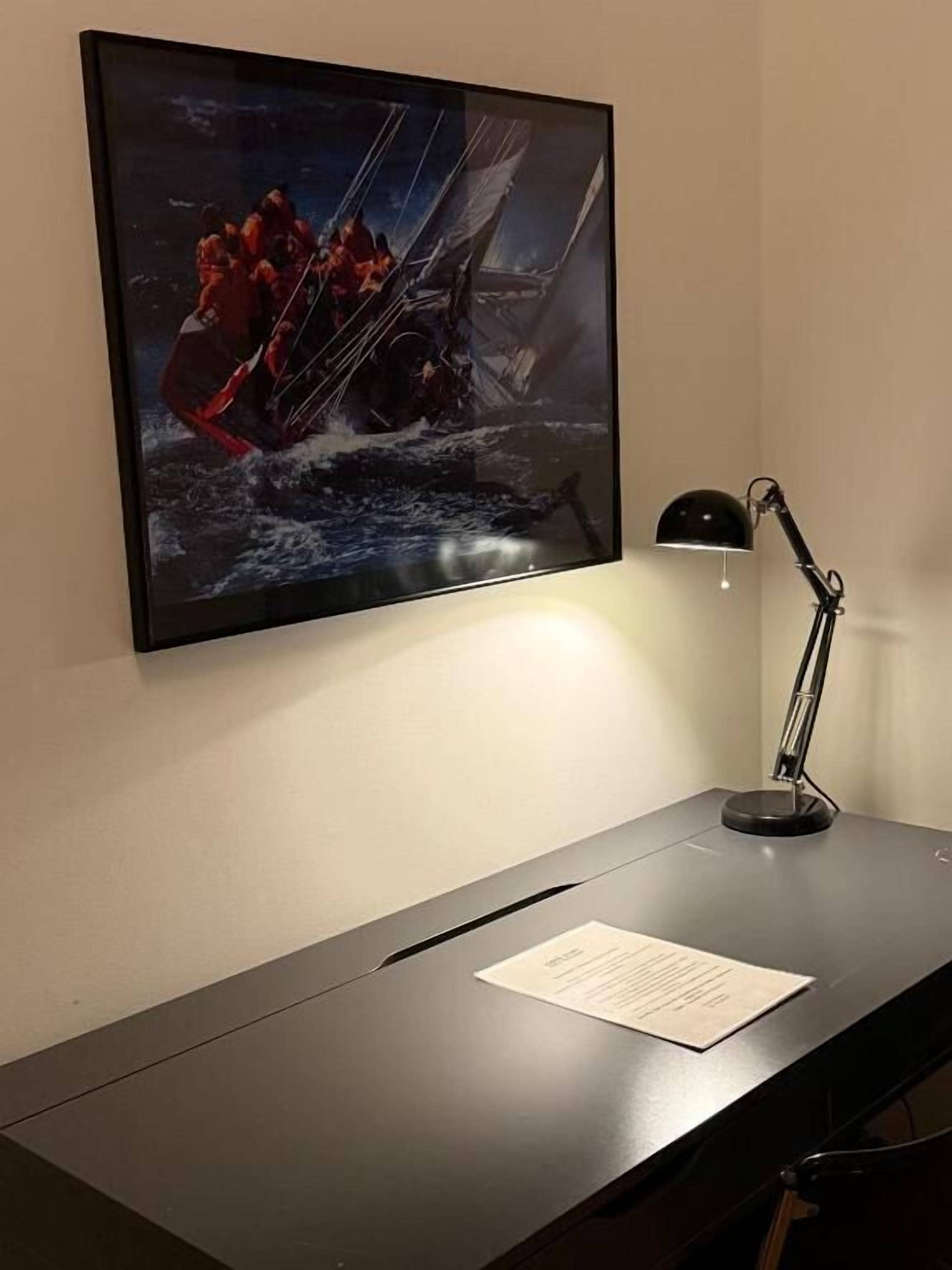 A desk with a framed artwork, a desk lamp, and a piece of paper.