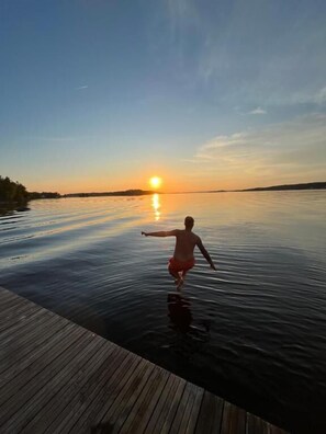 A person standing on a wooden dock extending over calm water during sunset. - Rindö Hamn Bed & Breakfast (Vaxholm)