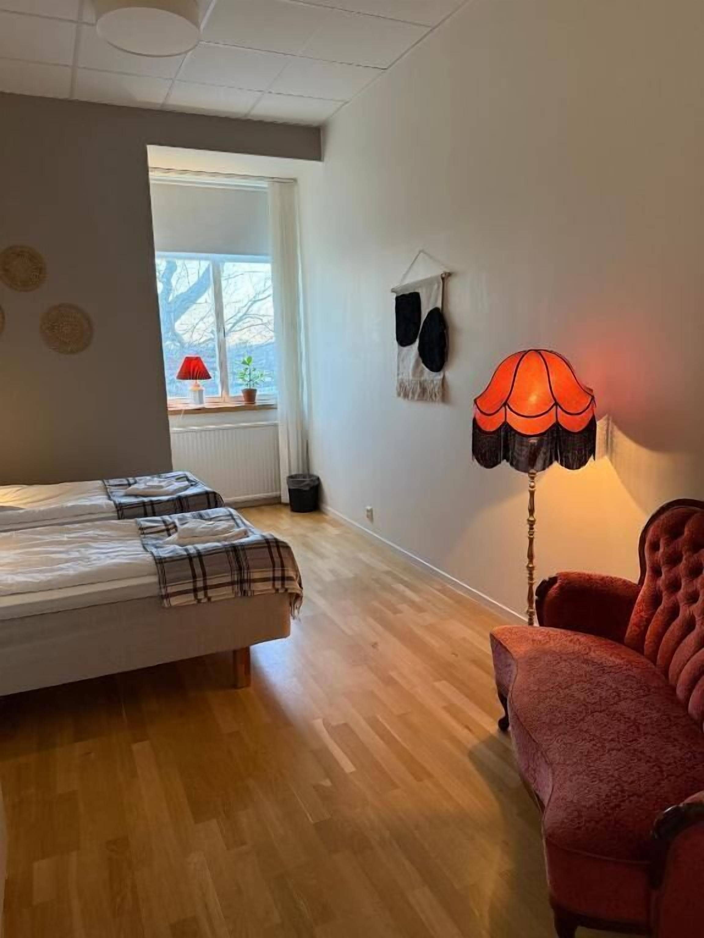 Una habitación con una cama, un sillón rojo, una lámpara y una ventana con vistas.