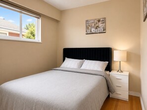 A bedroom with a bed, a nightstand, a lamp, a window, and a wall art piece. - Park View 3BR Home.Covered SunDeck. Near Metrotown (Vancouver)