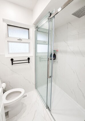 A modern bathroom with a glass shower enclosure, a toilet, and a window. - Park View 3BR Home.Covered SunDeck. Near Metrotown (Vancouver)