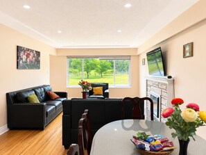 A living room with a black leather sofa, a dining table with a vase of flowers, and a fireplace. - Park View 3BR Home.Covered SunDeck. Near Metrotown (Vancouver)