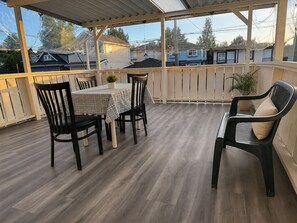 En täckt uteplats med ett bord och stolar, en krukväxt och utsikt över hus.