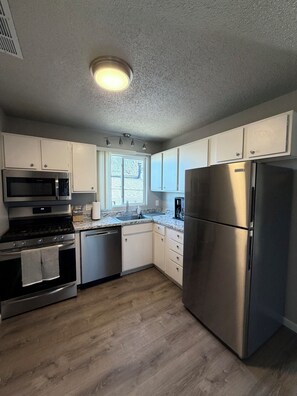A modern kitchen with stainless steel appliances, white cabinetry, and a window providing natural light. - The Workman’s Rest Pt. 2 No Cleaning Fee (Gillette)