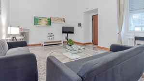 Una sala de estar moderna con una mesa de centro de vidrio, dos sofás grises, un radiador blanco y obras de arte en la pared.