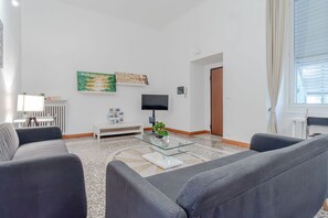 Ein modernes Wohnzimmer mit einem Glastisch, zwei grauen Sofas, einem weißen Heizkörper und Kunstwerken an der Wand.