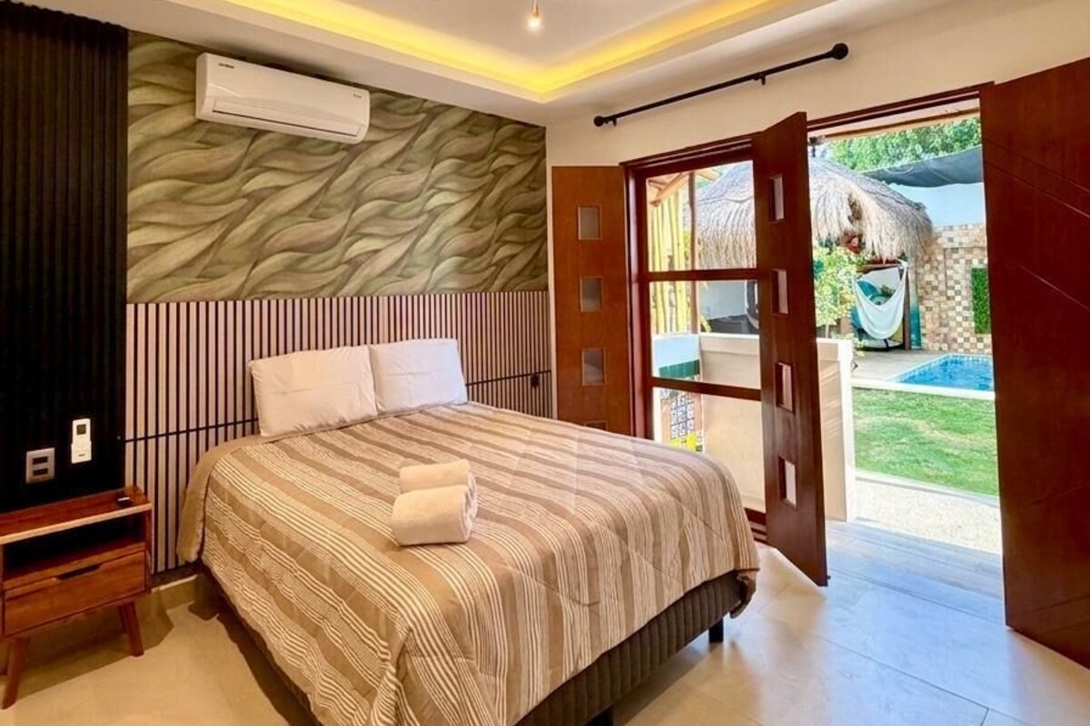 A bedroom with a bed, a ceiling fan, an air conditioning unit, a wooden door, and a view of an outdoor area.