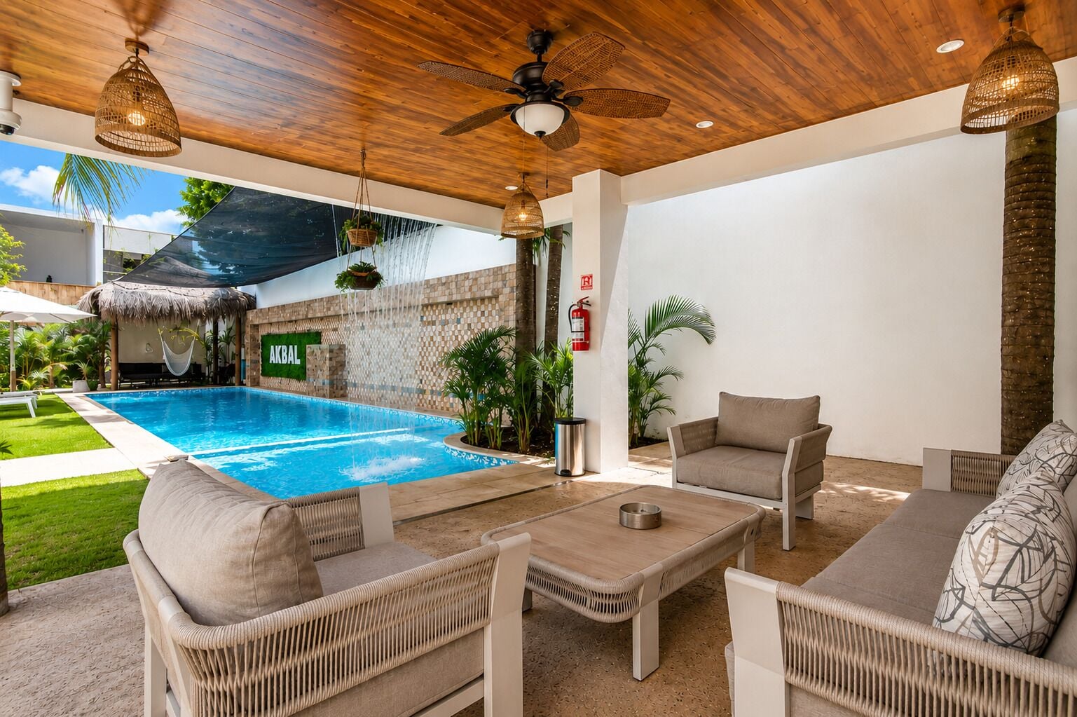 An outdoor pool area with wicker furniture, a ceiling fan, and a sign reading 'AKBAL'.