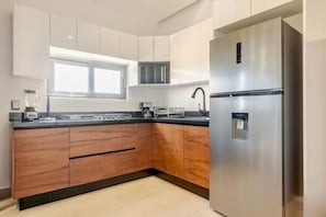 A modern kitchen with wooden cabinets, a stainless steel refrigerator, and a window providing natural light. - Akbal Cancun (Cancún)