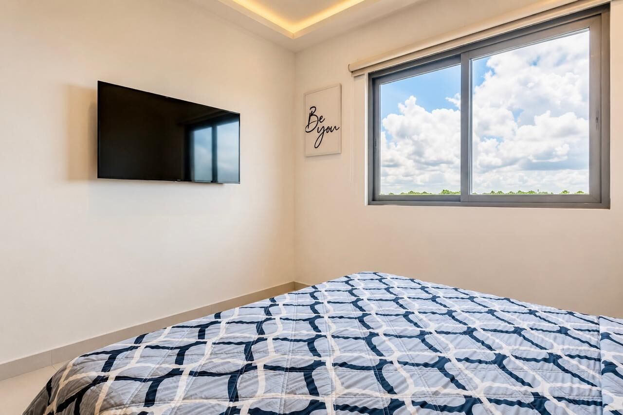 Een slaapkamer met een bed, een wandtelevisie, een raam met uitzicht op de lucht en een muur met een inspirerende quote.