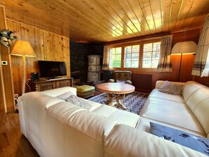 Ein gemütliches Wohnzimmer mit Holzboden, einem Fernseher, einem Steinkamin, einem runden Tisch und einem weißen Sofa.