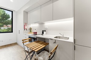 Een moderne keuken met witte kastjes, een roestvrijstalen spoelbak, een houten tafel en een raam met uitzicht op groen.