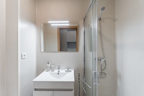 A bathroom with a glass-enclosed shower, a white sink, a mirror, and a light above the mirror. - GuestReady - Studio in São Mamede de Infesta (São Mamede de Infesta)