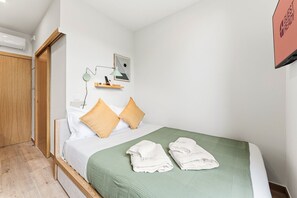 Hotelkamer met een bed, een groene plaid, twee kussens, een nachtkastje met een lamp, een wandplank met een telefoon en een bordje met de tekst 'Guest Ready'.