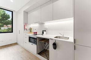A modern kitchen with white cabinetry, a built-in oven, a sink, and a window with a view of greenery. - GuestReady - Studio in São Mamede de Infesta (São Mamede de Infesta)