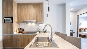 A modern kitchen with a built-in oven, stainless steel sink, and a dining area with a long table and chairs. - Bright and Modern Condo w/ Balcony, Shared Pool, A/c, Minutes to Beach & Town (Cabo San Lucas)