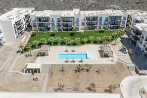A modern hotel with multiple balconies, a central swimming pool, and a landscaped area with palm trees. - Bright and Modern Condo w/ Balcony, Shared Pool, A/c, Minutes to Beach & Town (Cabo San Lucas)