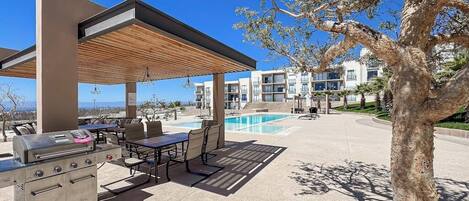 Un patio exterior con una parrilla, asientos y una piscina.