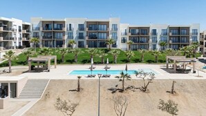 A modern hotel with multiple floors, a swimming pool, and palm trees. - Bright and Modern Condo w/ Balcony, Shared Pool, A/c, Minutes to Beach & Town (Cabo San Lucas)