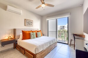 Camera da letto con letto, comodino, lampada da comodino, ventilatore a soffitto, ampia finestra e vista sugli edifici esterni.