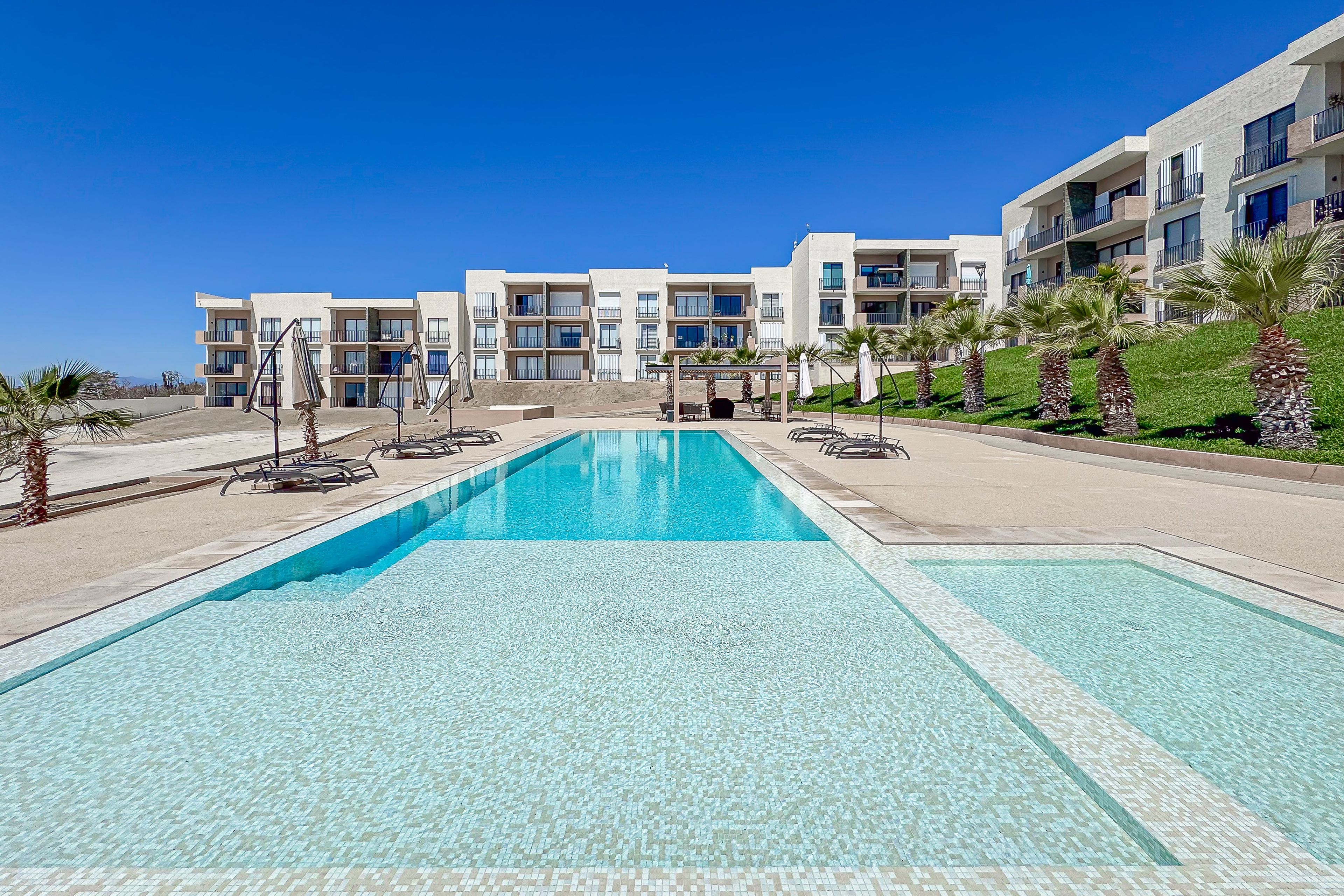 Un hôtel moderne doté d’une grande piscine, de nombreux balcons et de palmiers.