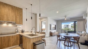 A modern kitchen with wooden cabinets, a central island, and a dining area with a round table and chairs. - Bright and Modern Condo w/ Balcony, Shared Pool, A/c, Minutes to Beach & Town (Cabo San Lucas)