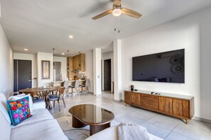 A modern living room with a sofa, coffee table, and a TV mounted on the wall. - Bright and Modern Condo w/ Balcony, Shared Pool, A/c, Minutes to Beach & Town (Cabo San Lucas)
