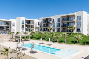 Un hotel moderno con piscina, area salotto esterna e palme.