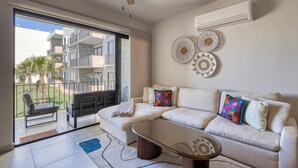 A modern living room with a sofa, coffee table, and decorative wall art. - Bright and Modern Condo w/ Balcony, Shared Pool, A/c, Minutes to Beach & Town (Cabo San Lucas)